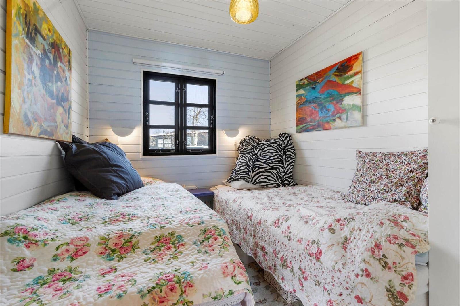 Zwei Betten mit floralen Bettdecken, Wandbilder und ein Fenster mit schwarzen Rahmen.