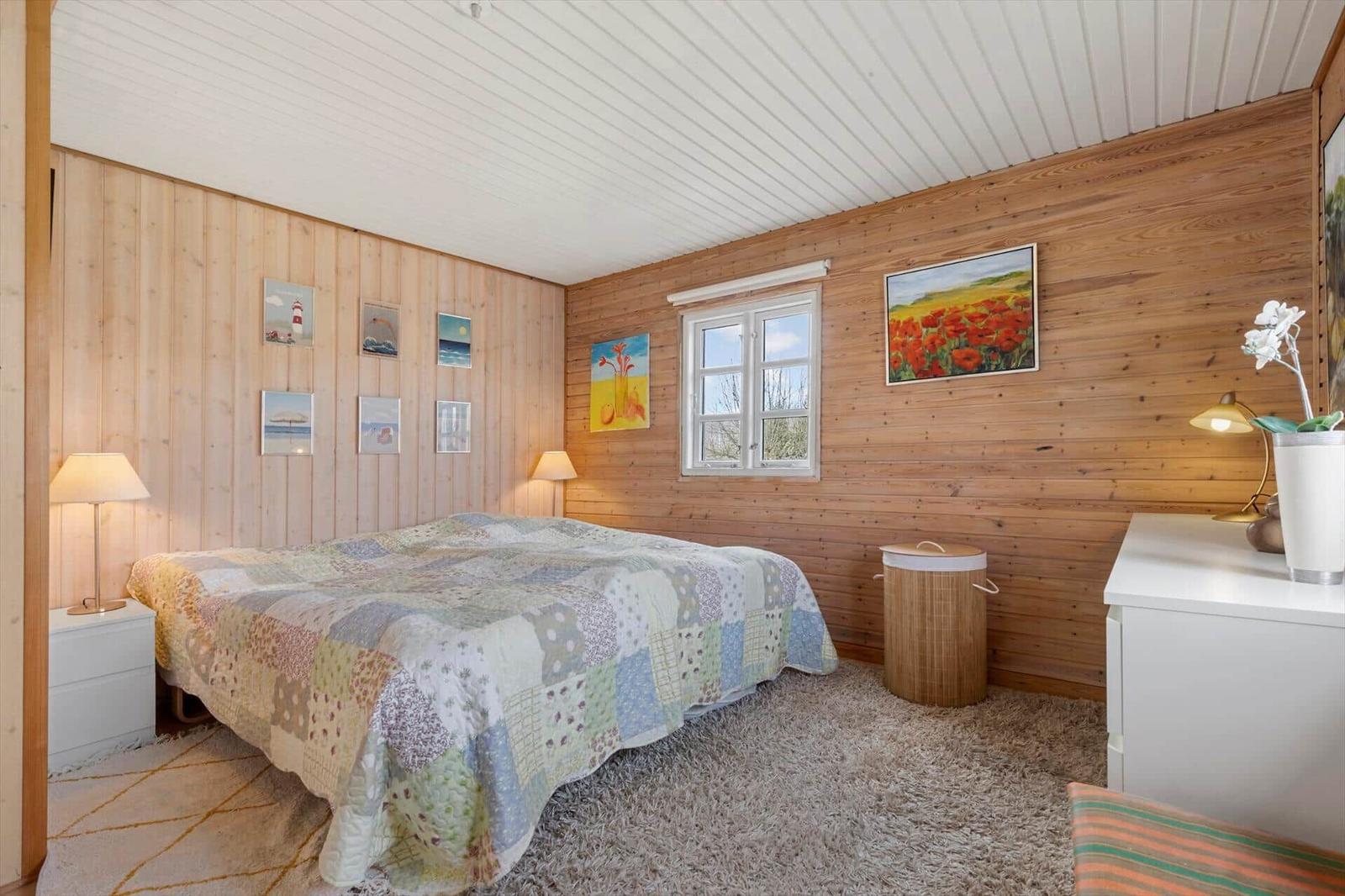 Schlafzimmer mit Holzwand, Bett, Fenster und Kunstwerken.