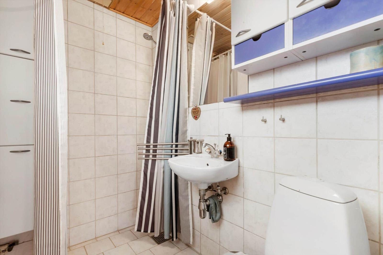 Badezimmer mit Waschbecken, Dusche und Toilette. Weiße Fliesen und Holzdecke.