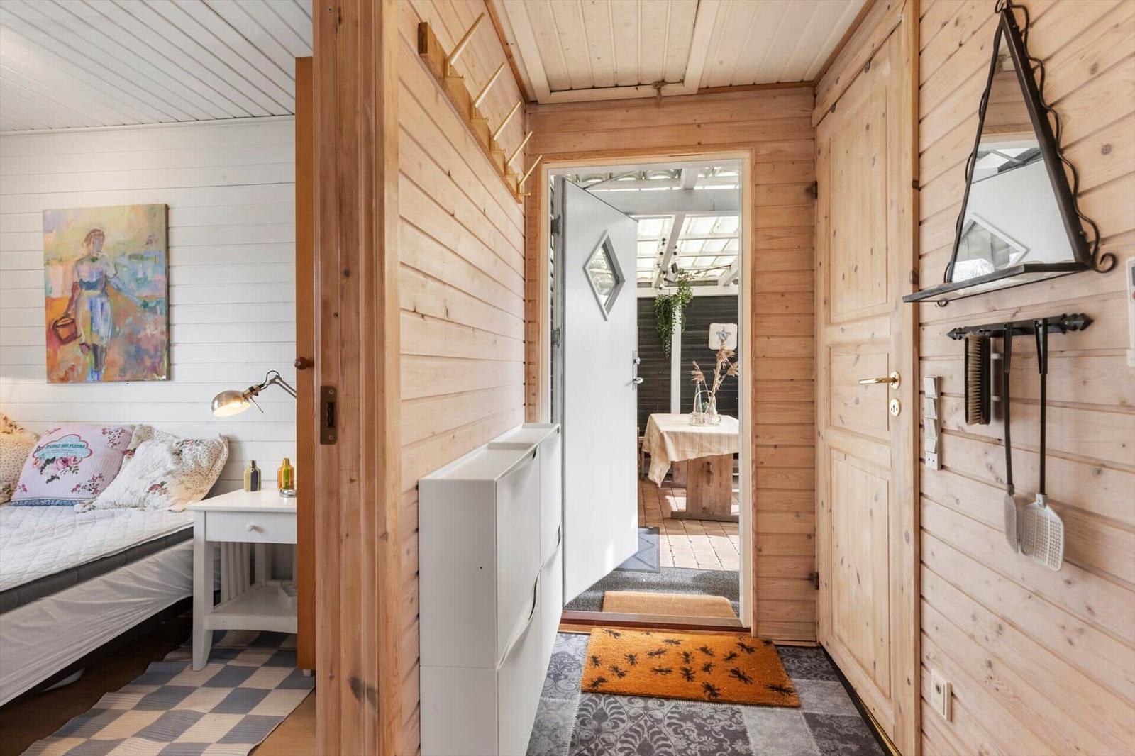 Schlafzimmer mit Bett und Wandbild. Flur führt zur Terrasse. Holzwände und Tür.