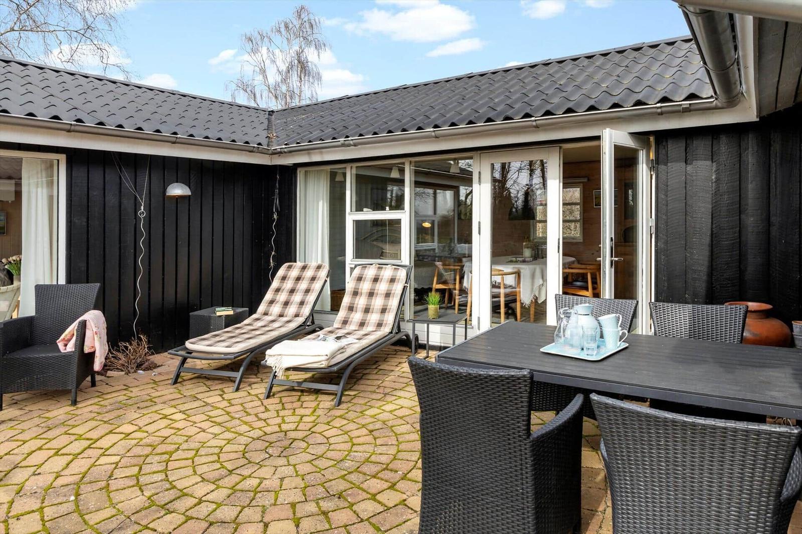 Terrasse mit Liegen, Tisch und Stühlen. Durchgehende Glasfront zum Innenraum.