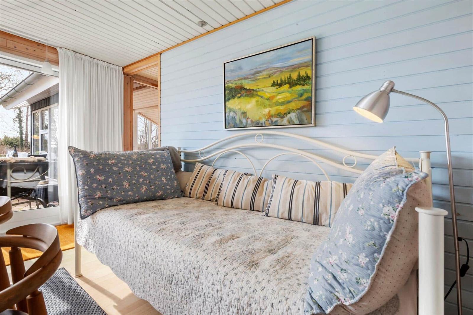 Ein Bett mit Kissen und Decke an einer blauen Wand mit Gemälde und Stehlampe.