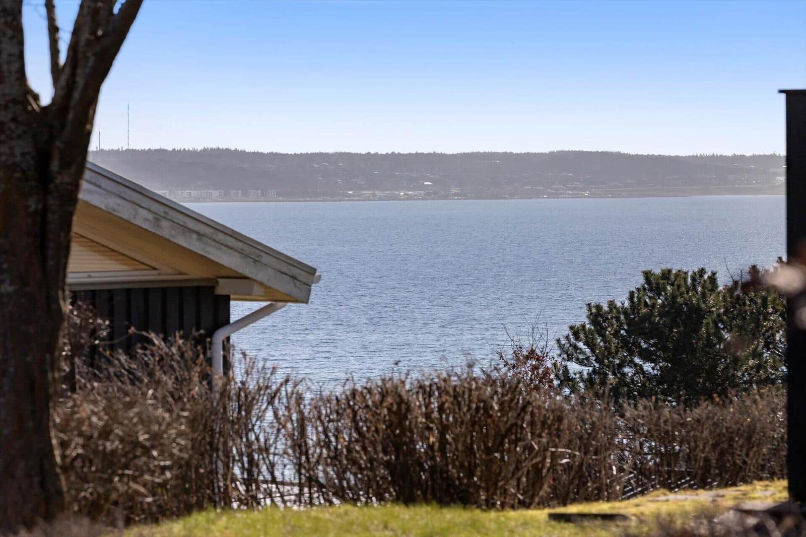 Haus mit Blick auf ruhiges Wasser und bewaldeten Hügeln im Hintergrund.
