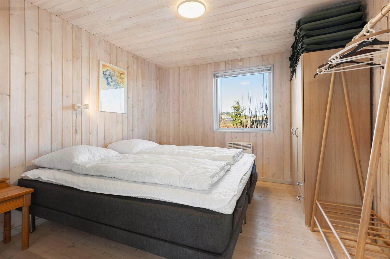 Schlafzimmer mit Holzwand, Bett, Kleiderschrank und Fenster mit Blick.