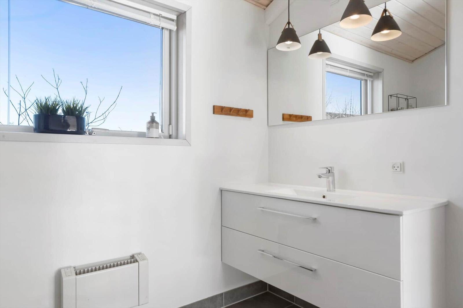 Badezimmer mit Waschbecken, Spiegel und Fenster mit Pflanze.