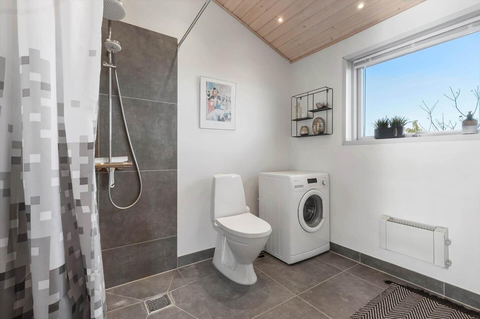 Bad mit Dusche, Toilette und Waschmaschine. Fenster mit Pflanzen und Holzdecke.