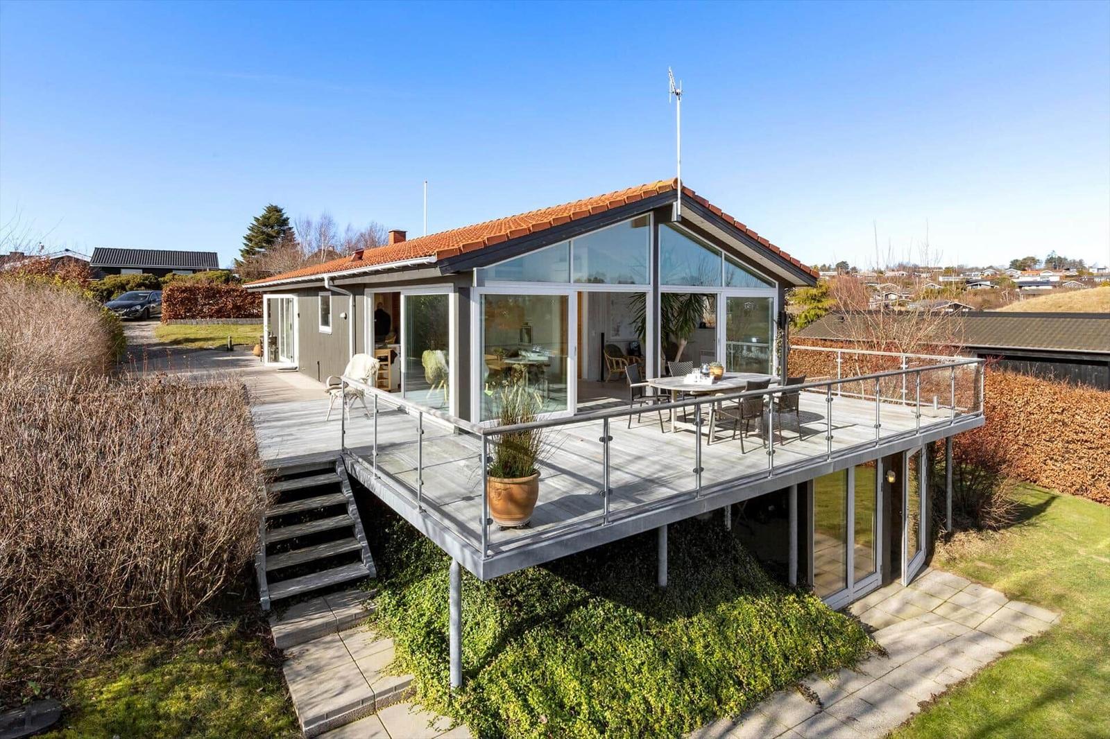 Moderne Villa mit großem Balkon, Glasfront und Terrasse mit Sitzgelegenheit.
