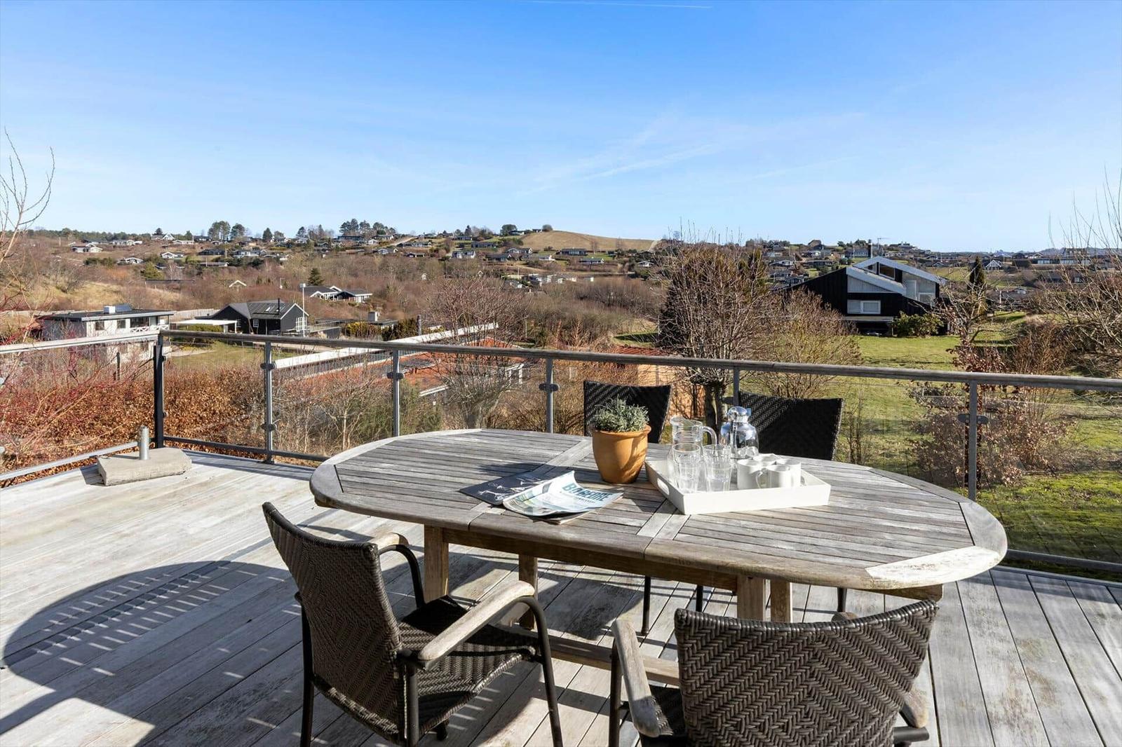 Terrasse mit Tisch und Stühlen, Blick auf Hügellandschaft mit Häusern.
