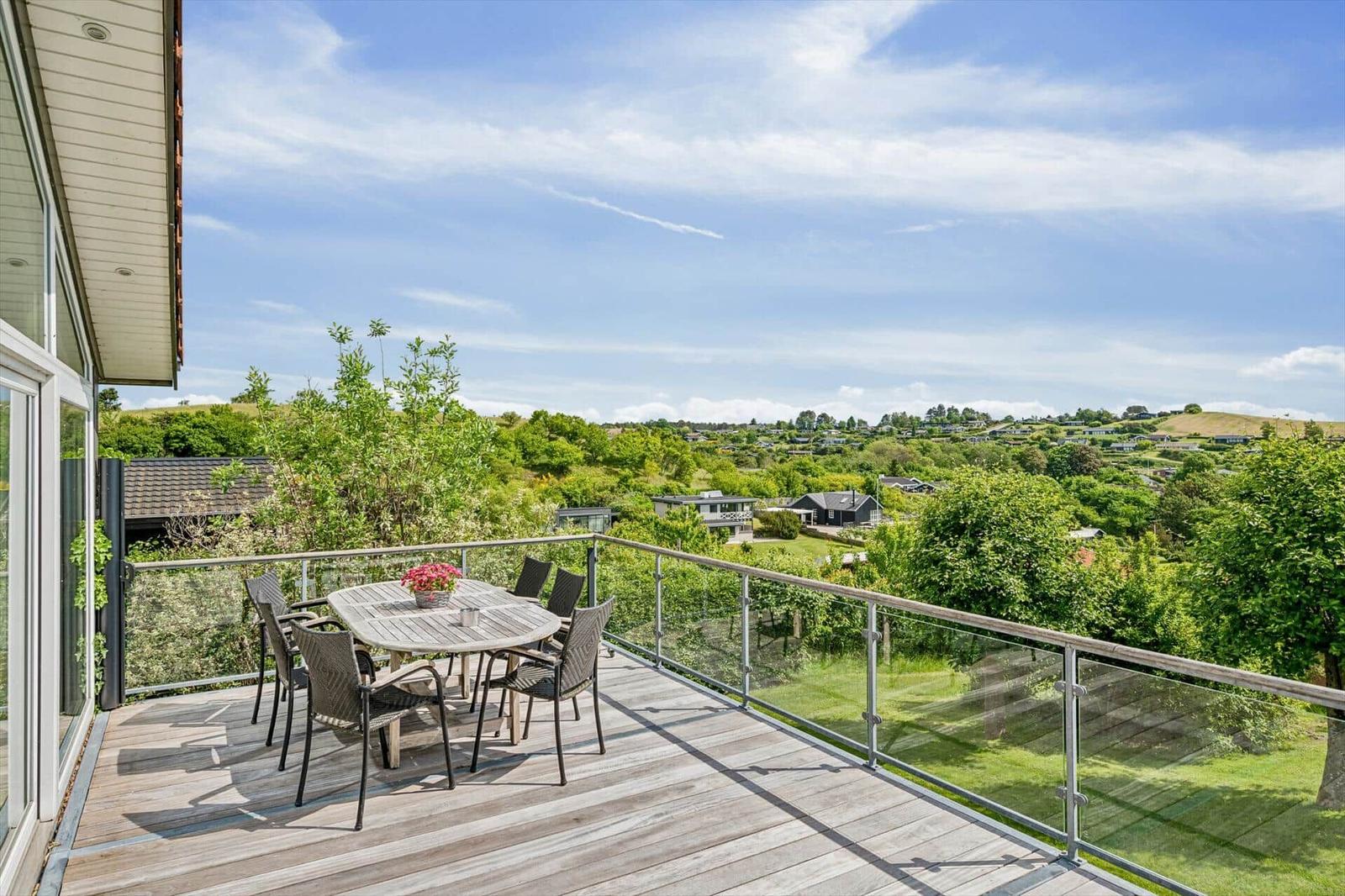 Terrasse mit Tisch und Stühlen, Blick auf grüne Landschaft und Häuser.
