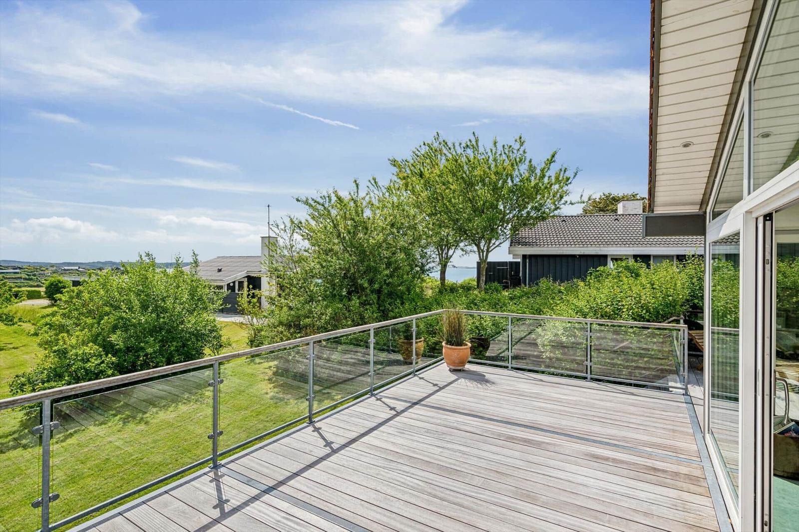 Terrasse mit Glasgeländer und Blick auf grüne Landschaft und Haus.