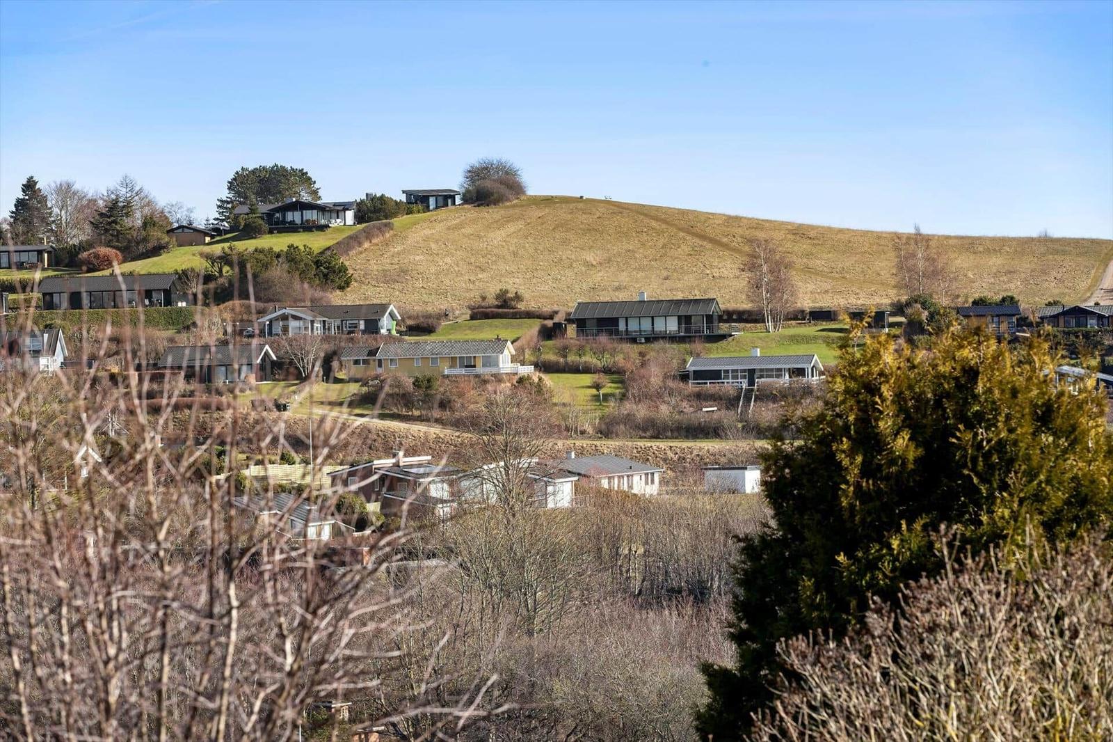 Hügelige Landschaft mit mehreren Häusern und Bäumen unter blauem Himmel.
