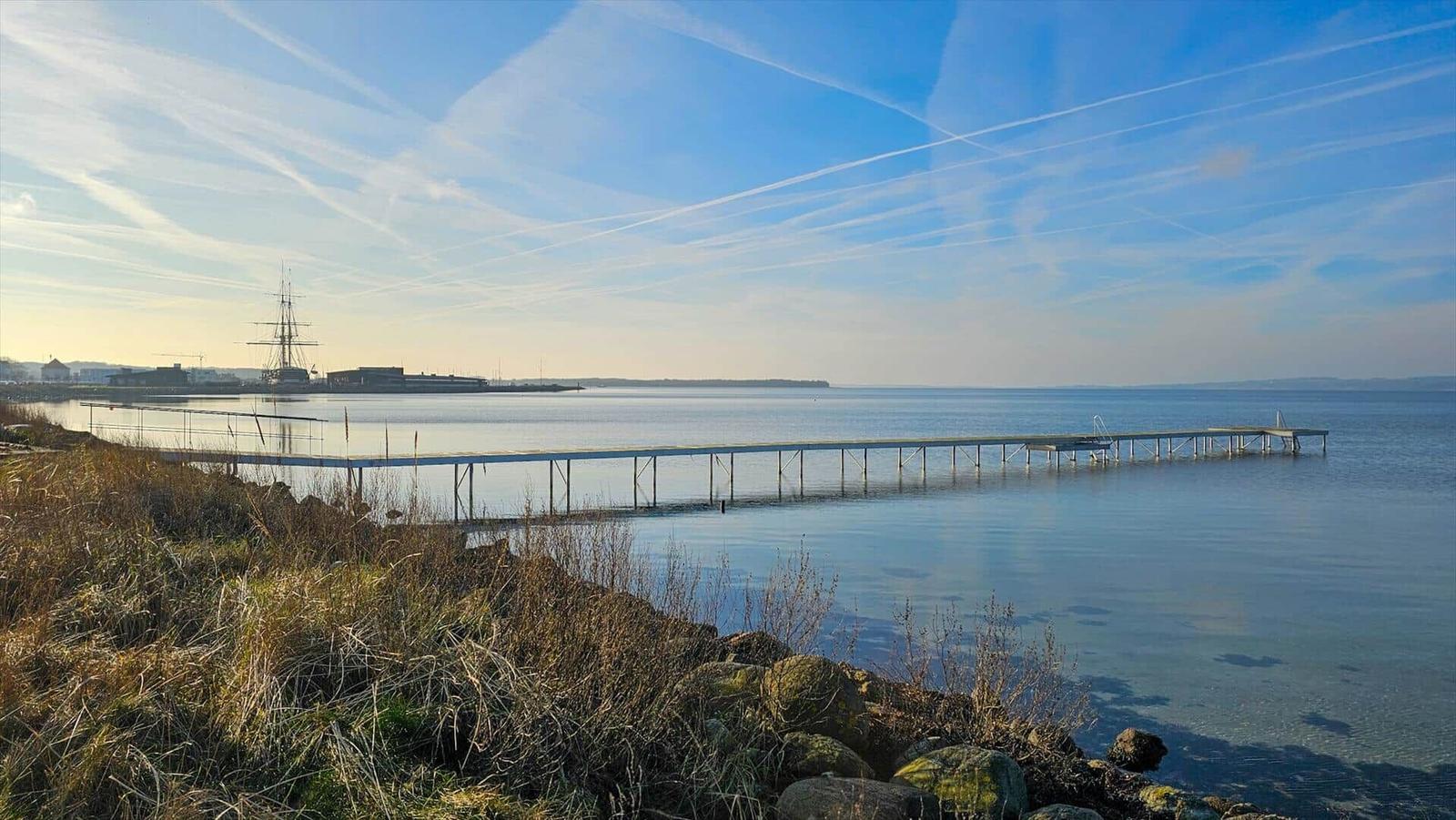 Langer Steg führt ins Wasser. Im Hintergrund ist ein Schiff zu sehen.
