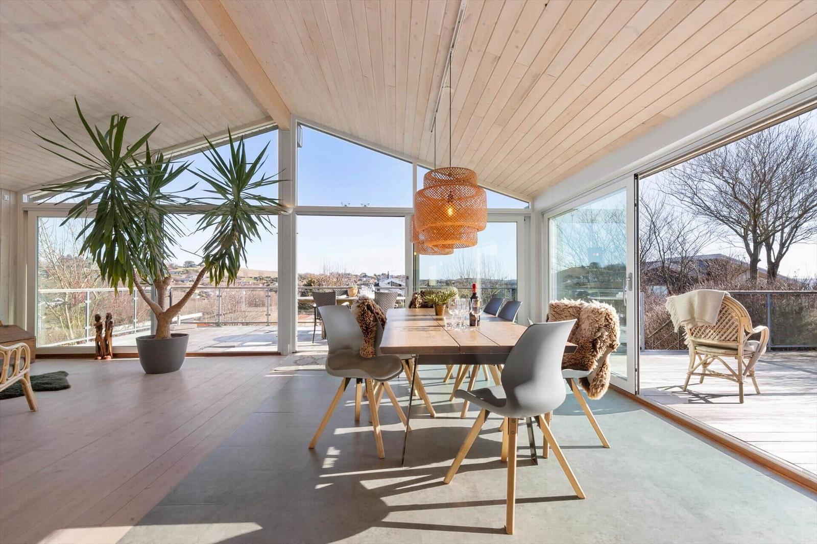 Essbereich mit Tisch, Stühlen und Pflanze. Große Fenster und Terrasse mit Sicht auf Landschaft.