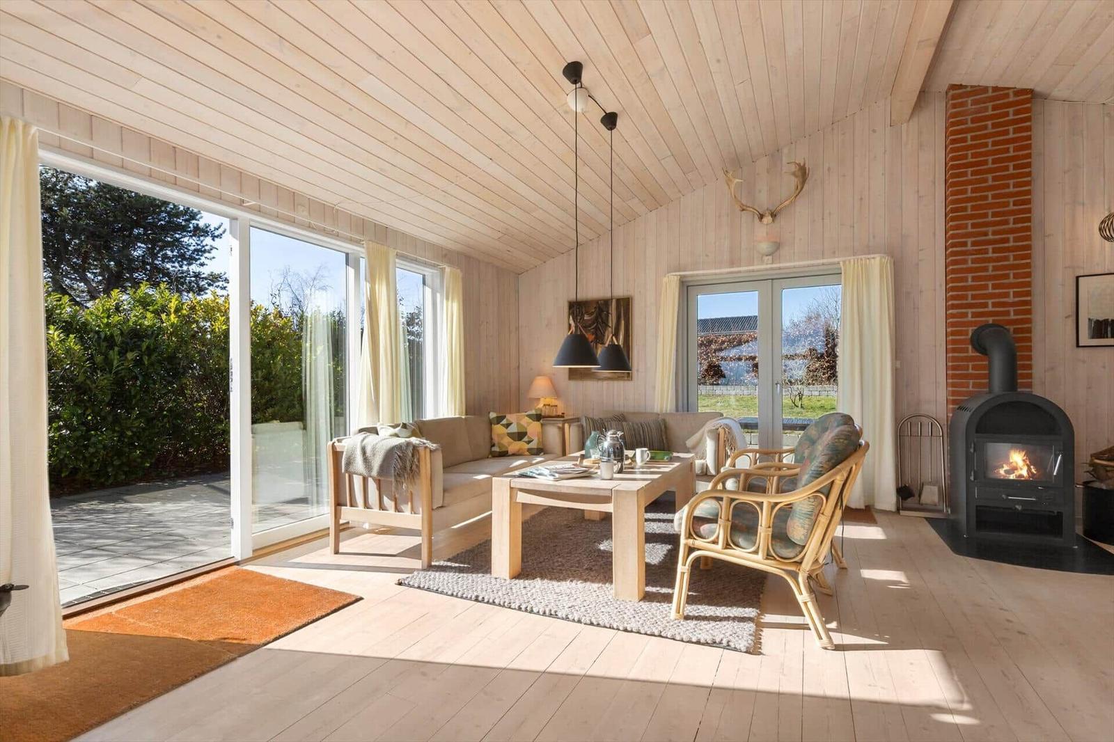 Wohnraum mit Holzdecke, Kamin und Glasfront zur Terrasse.