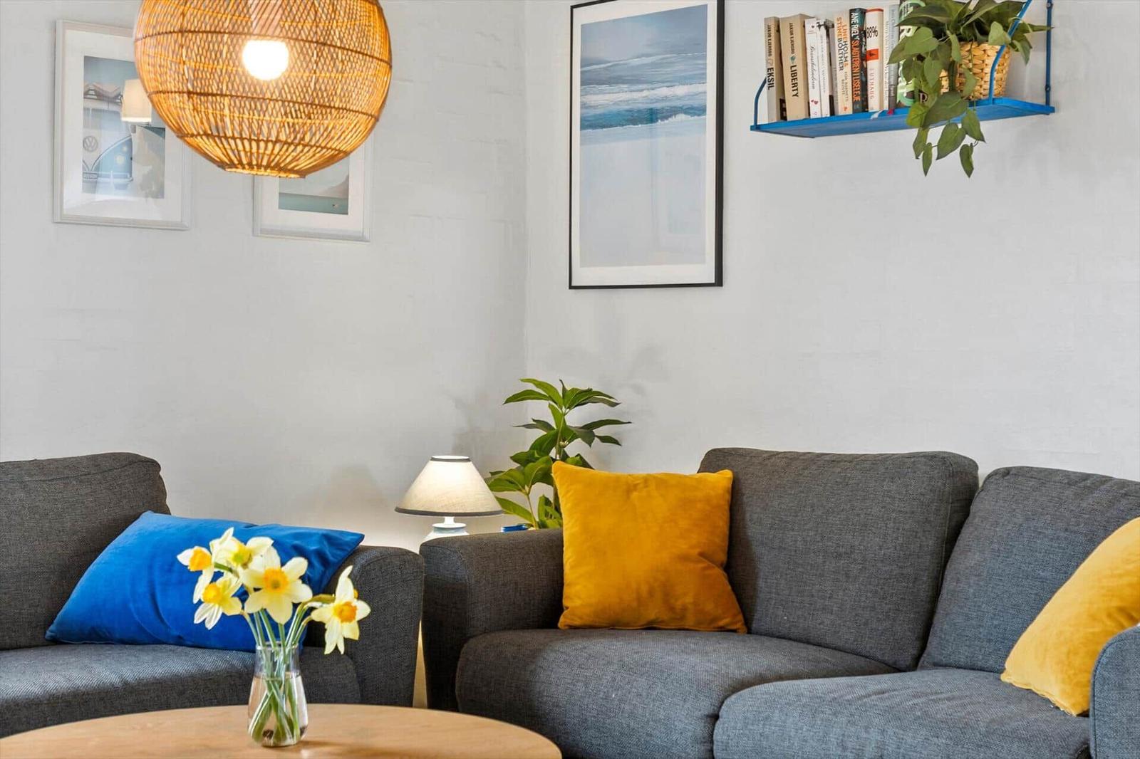 Grauer Sofa mit blauen und gelben Kissen, Wandbild und Lampe