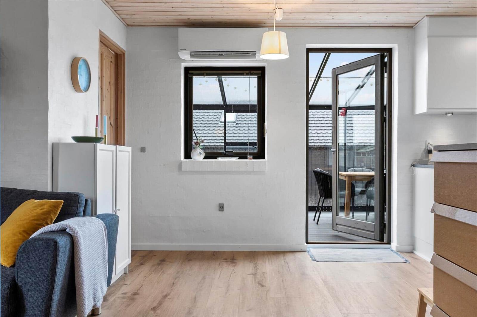 Wohnraum mit Sofa, Fenster und Glastür zum Balkon.