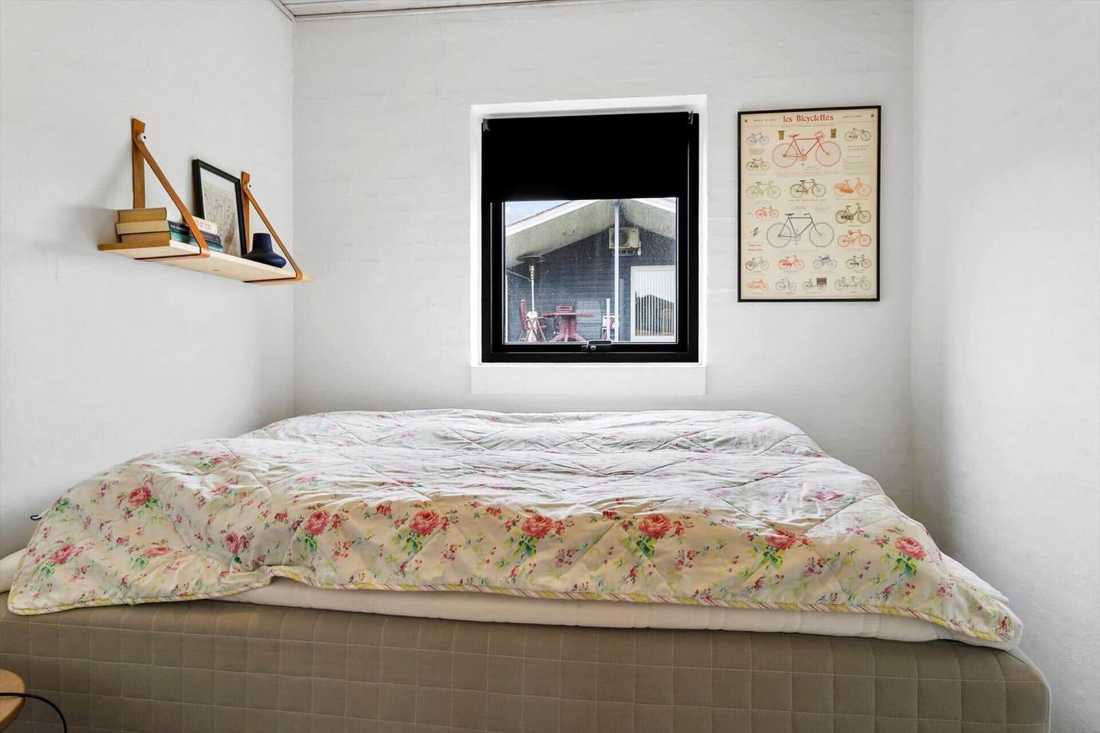 Schlafzimmer mit Bett, Fenster und Wandbild. Regal mit Büchern und Dekoration.