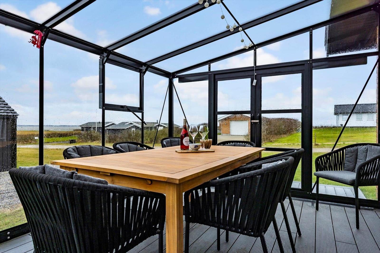 Terrassenbereich mit Tisch und Stühlen, Blick auf Grünfläche und Himmel.