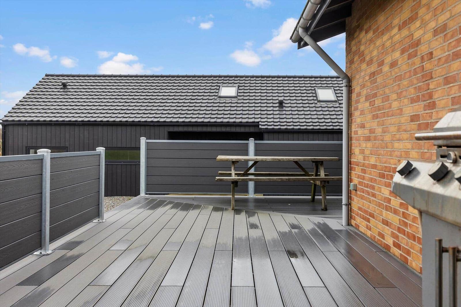 Terrasse mit Picknicktisch und Grill, Blick auf das Haus mit Dachfenstern.