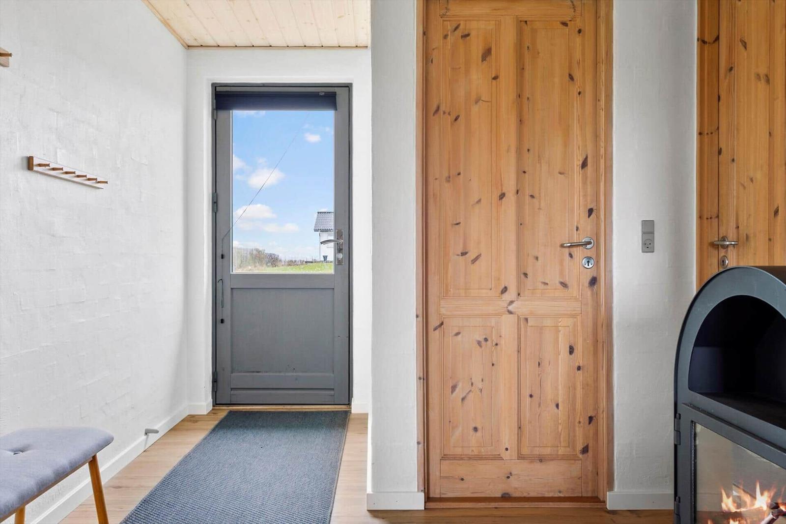 Eingangsbereich mit Holztür, Fenster und Kaminofen. Boden aus Holz, Wandfarbe Weiß.