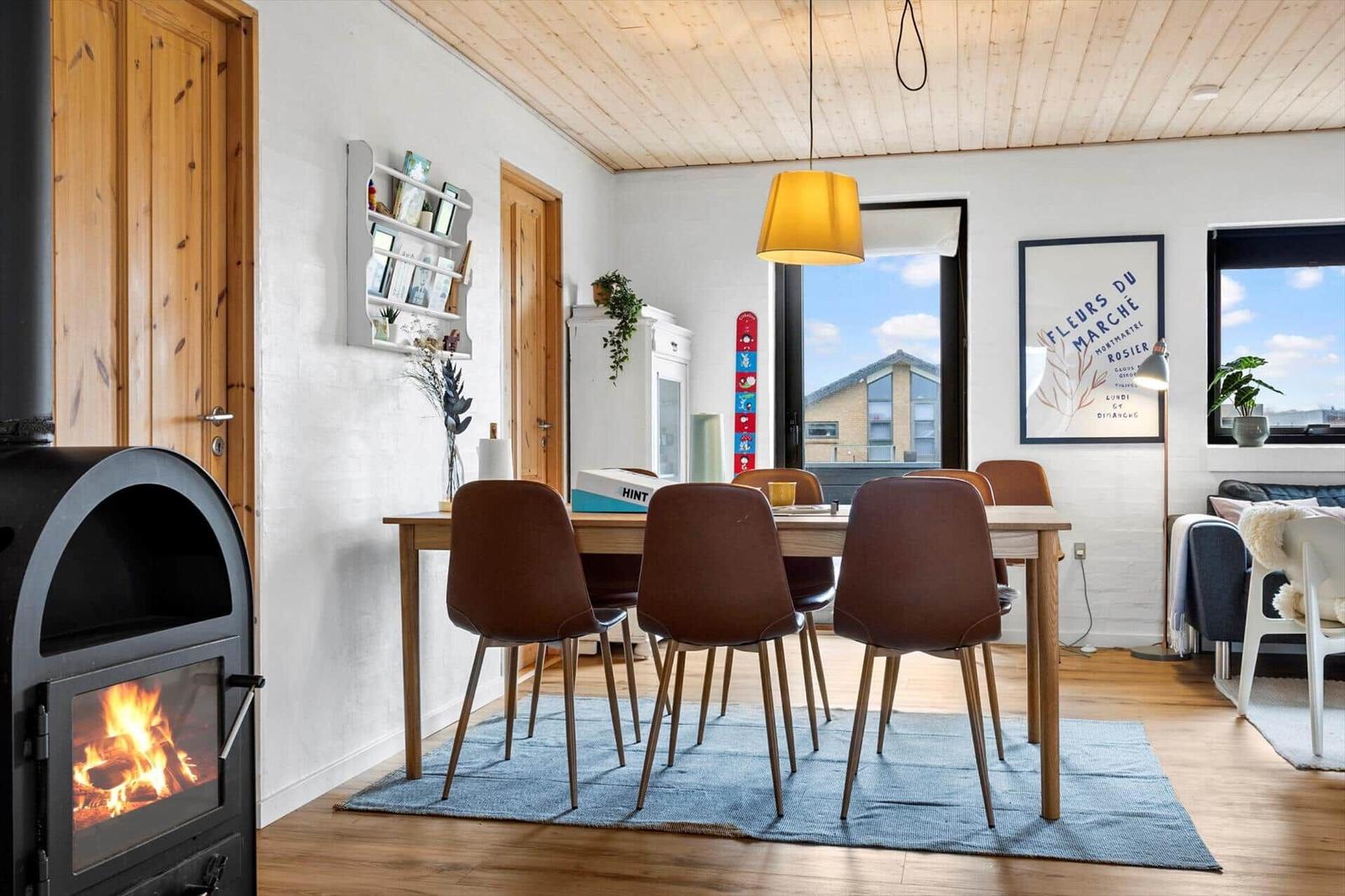 Essbereich mit Tisch, Stühlen und Kaminofen. Holzdecke und große Fenster.