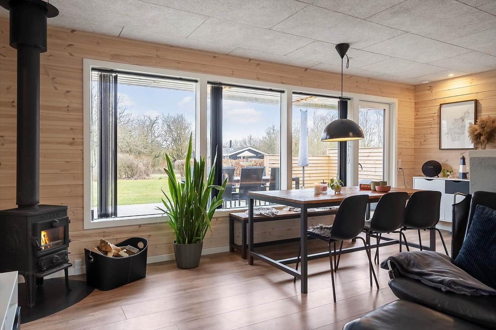 Wohn- und Essbereich mit Holzwand, Kamin und großem Fensterblick auf Garten.