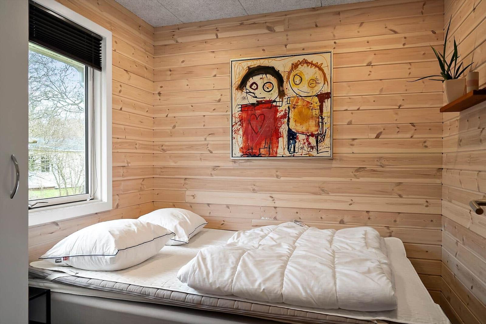 Schlafzimmer mit Holzwand, Bett, Fenster und Wandbild.
