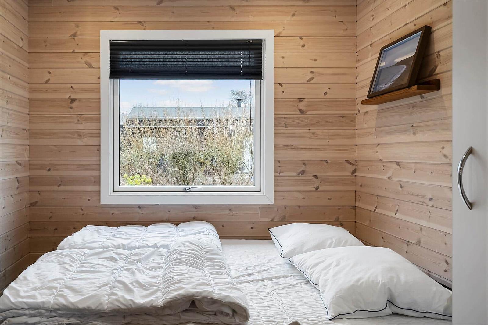 Schlafzimmer mit Holzwänden, Bett und Fenster mit Blick nach draußen.