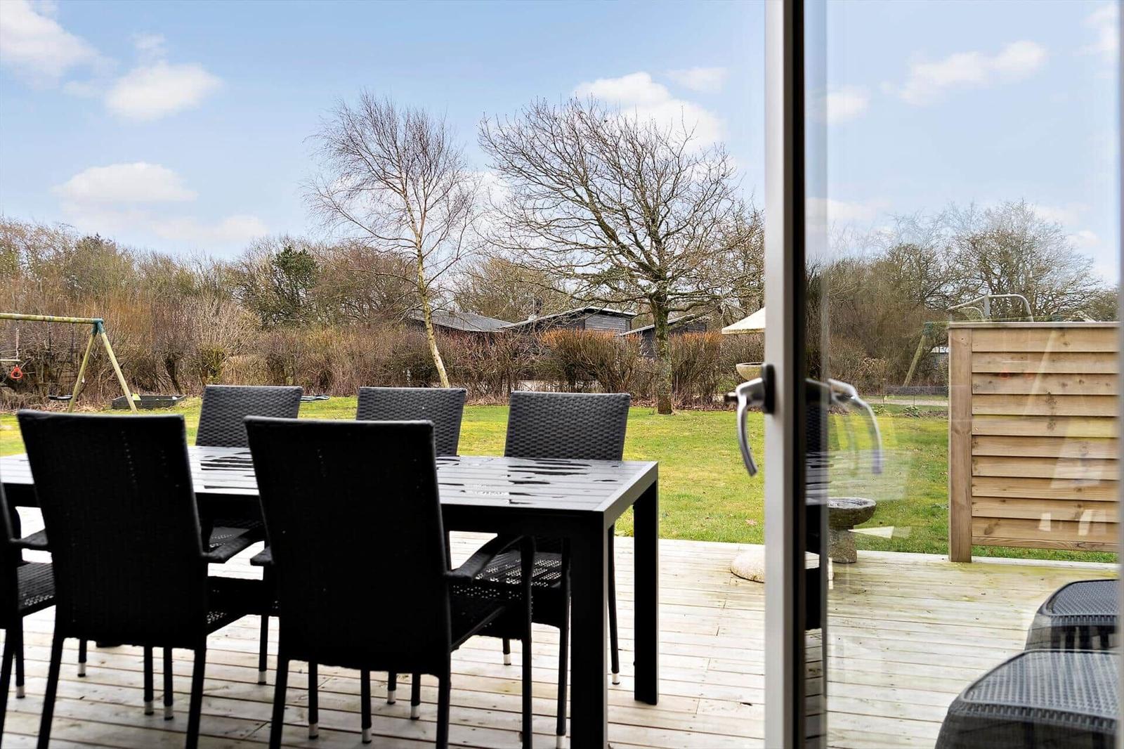 Terrasse mit Tisch und Stühlen, Blick auf Garten und Bäume.