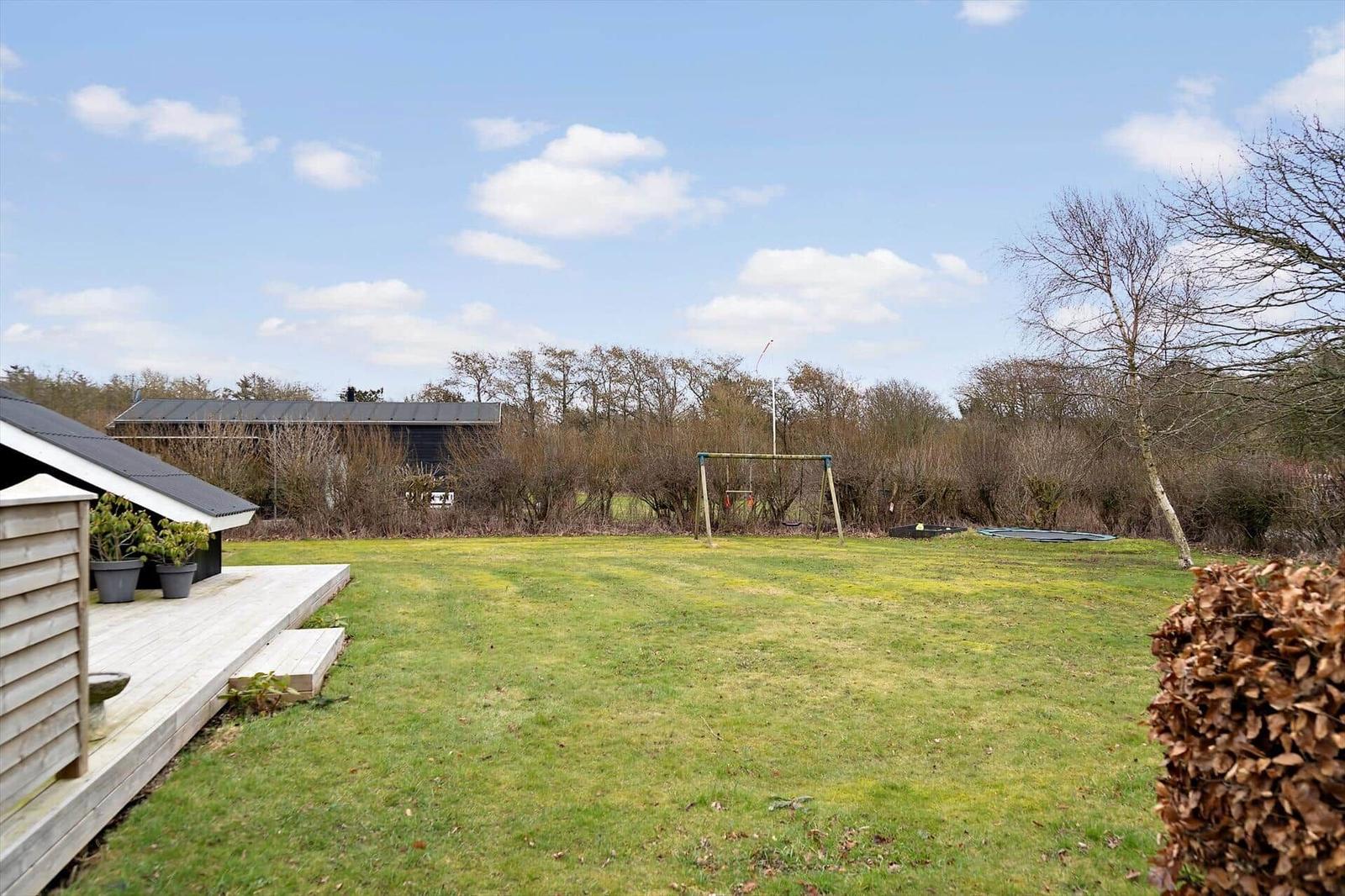 Großer Garten mit Spielplatz, Holzterrasse und Blick auf Wald.