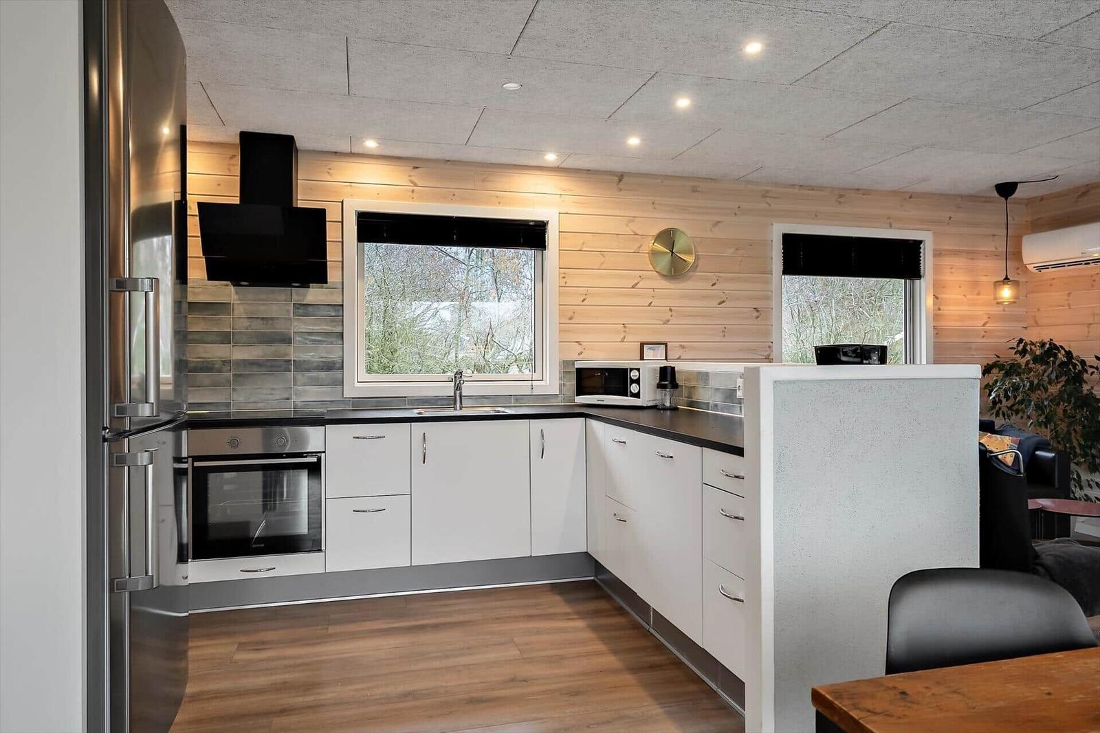 Küche mit weißen Schränken, Edelstahlgeräten und Holzwand.