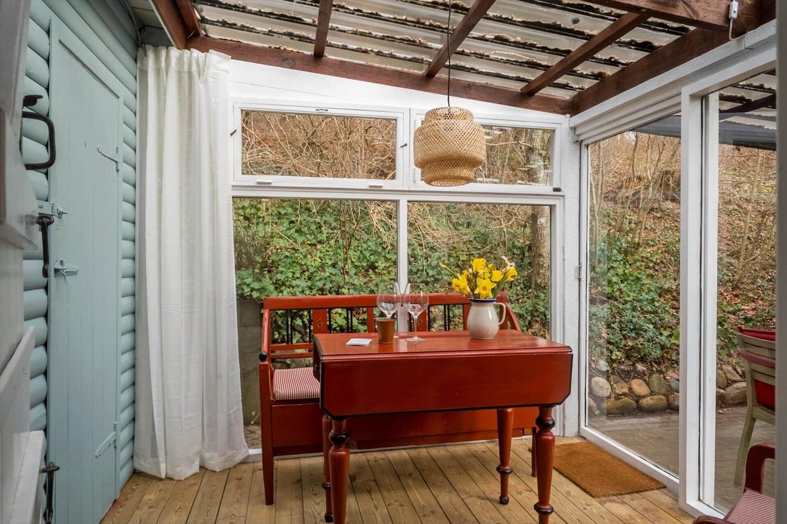 Roter Tisch mit Stuhl und Blumen vor Fenster mit Blick auf Garten.