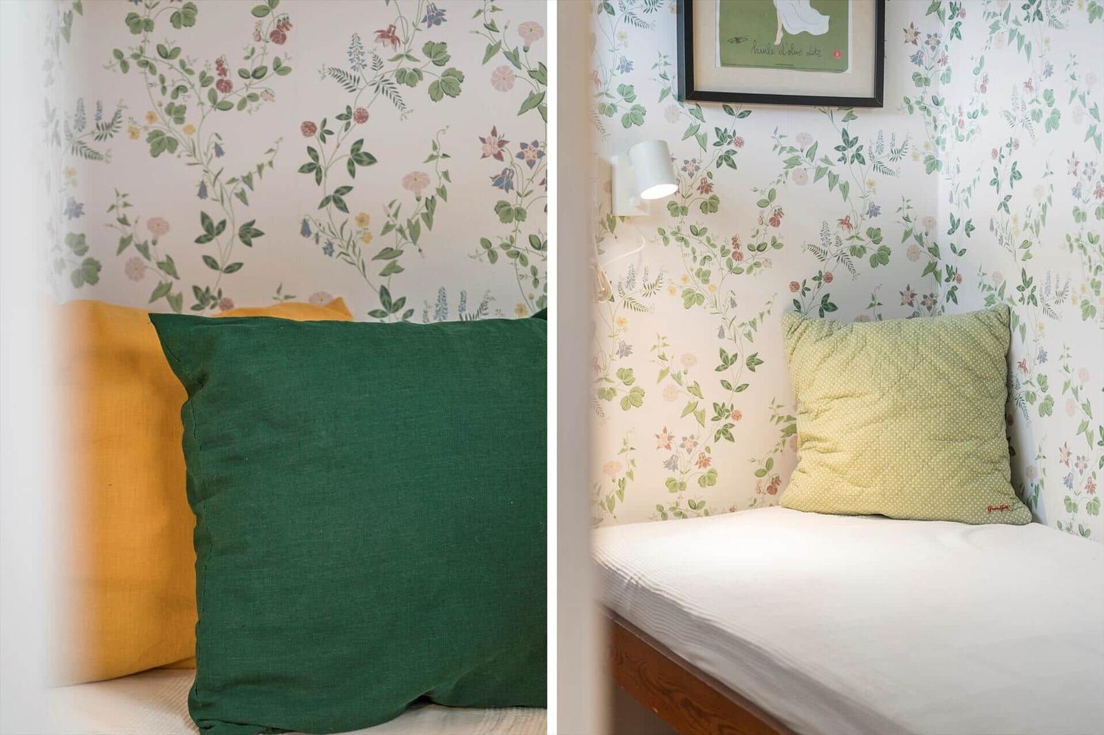Schlafzimmer mit floraler Tapete, Kissen und Wandlampe.