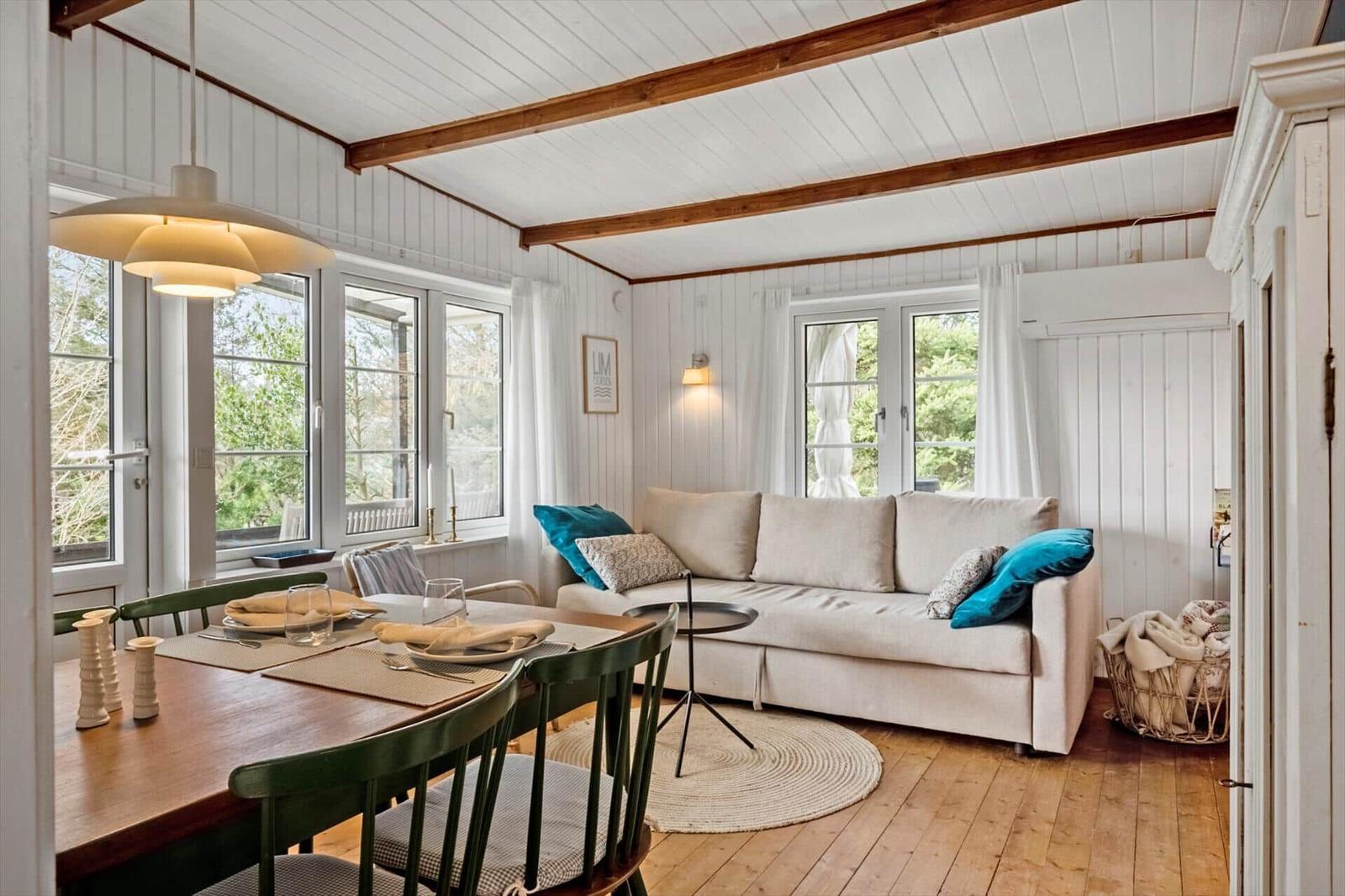 Wohn- und Essbereich mit Sofa, Tisch und Stühlen. Holzdielen und weiße Wände.