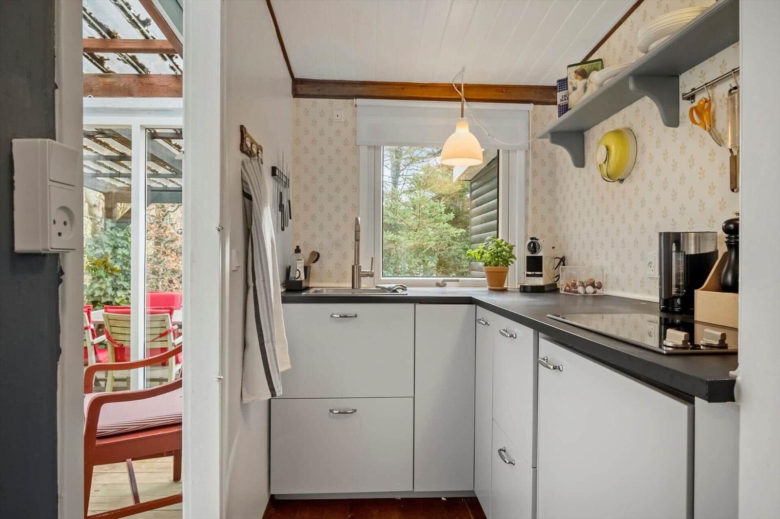 Küche mit weißen Schränken, dunkler Arbeitsplatte und Fensterblick auf Garten.