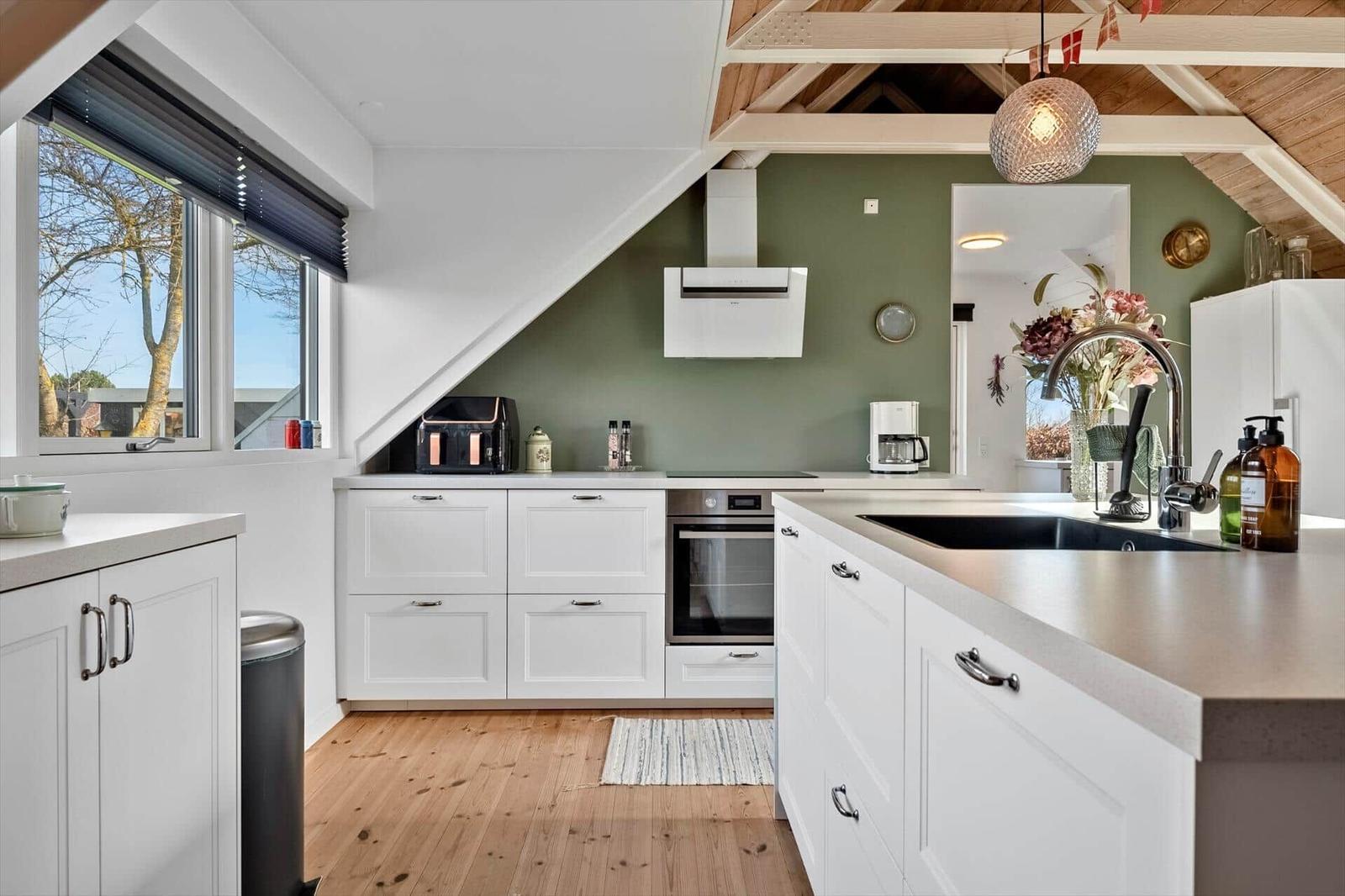 Küche mit weißer Einbauküche, Holzboden und grüner Wand