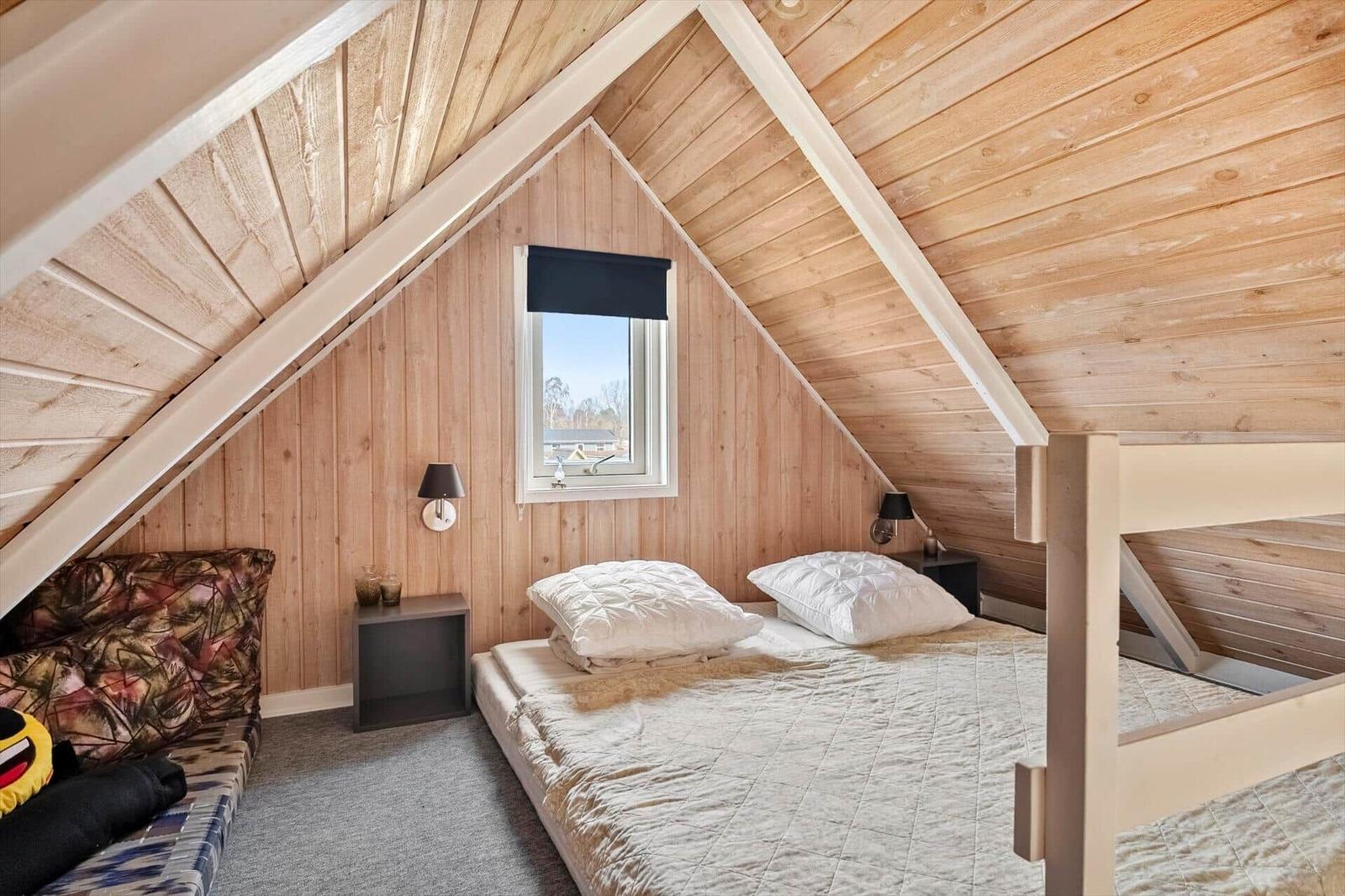 Schlafzimmer mit Doppelbett, Fenster und Holzwandverkleidung.