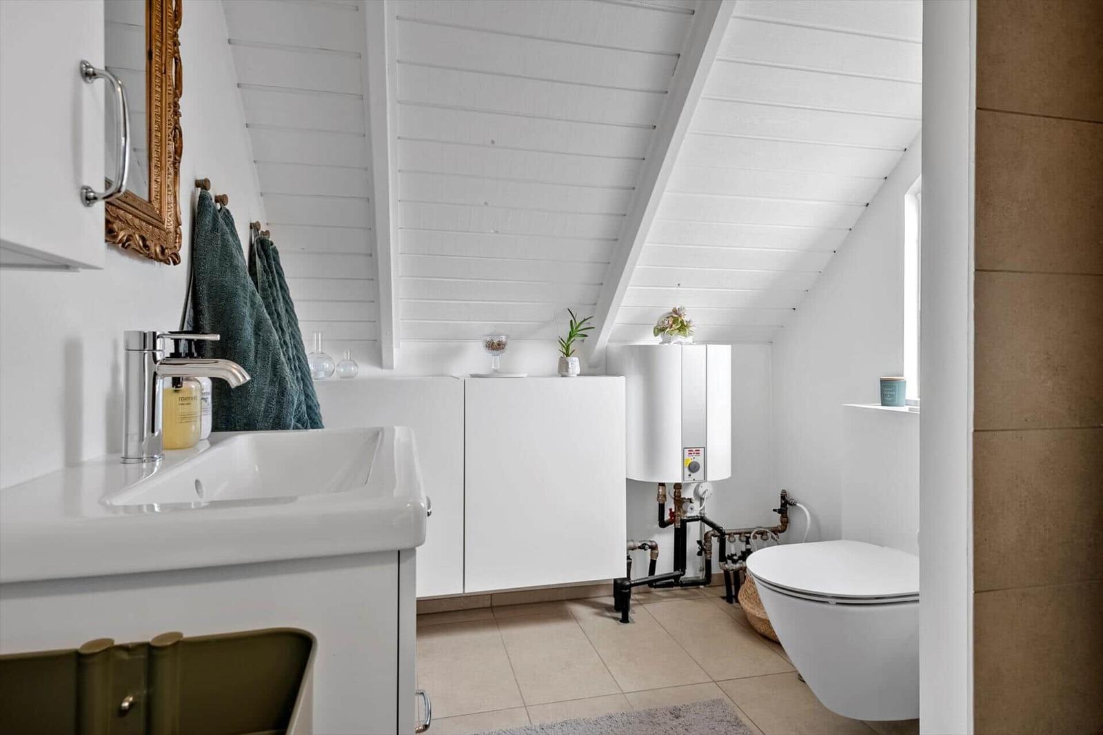 Badezimmer mit Waschbecken, Toilette und Heizung unter schrägem Dach
