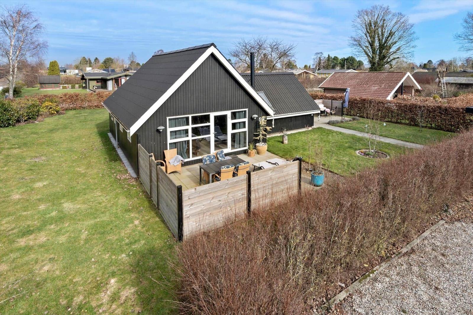 Schwarzes Haus mit Terrasse und Garten. Holzgeländer und Pflanzen sind sichtbar.