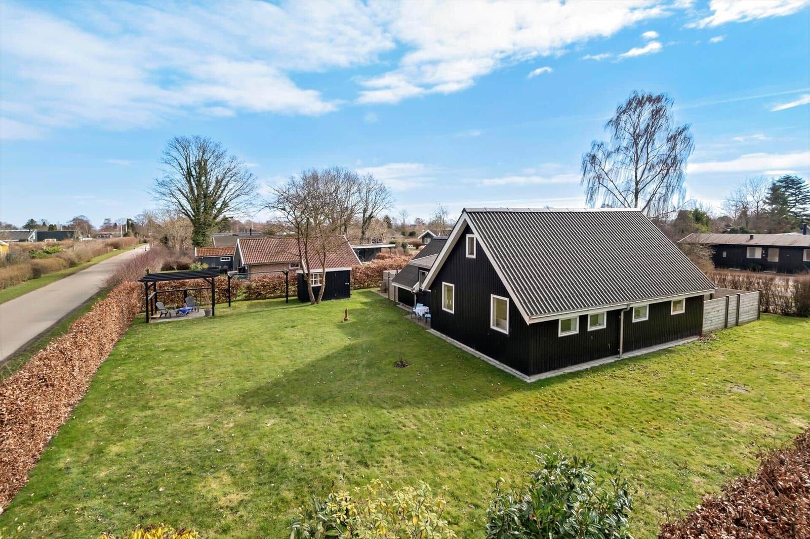 Schwarzes Haus mit großem Garten und Terrasse unter blauem Himmel.