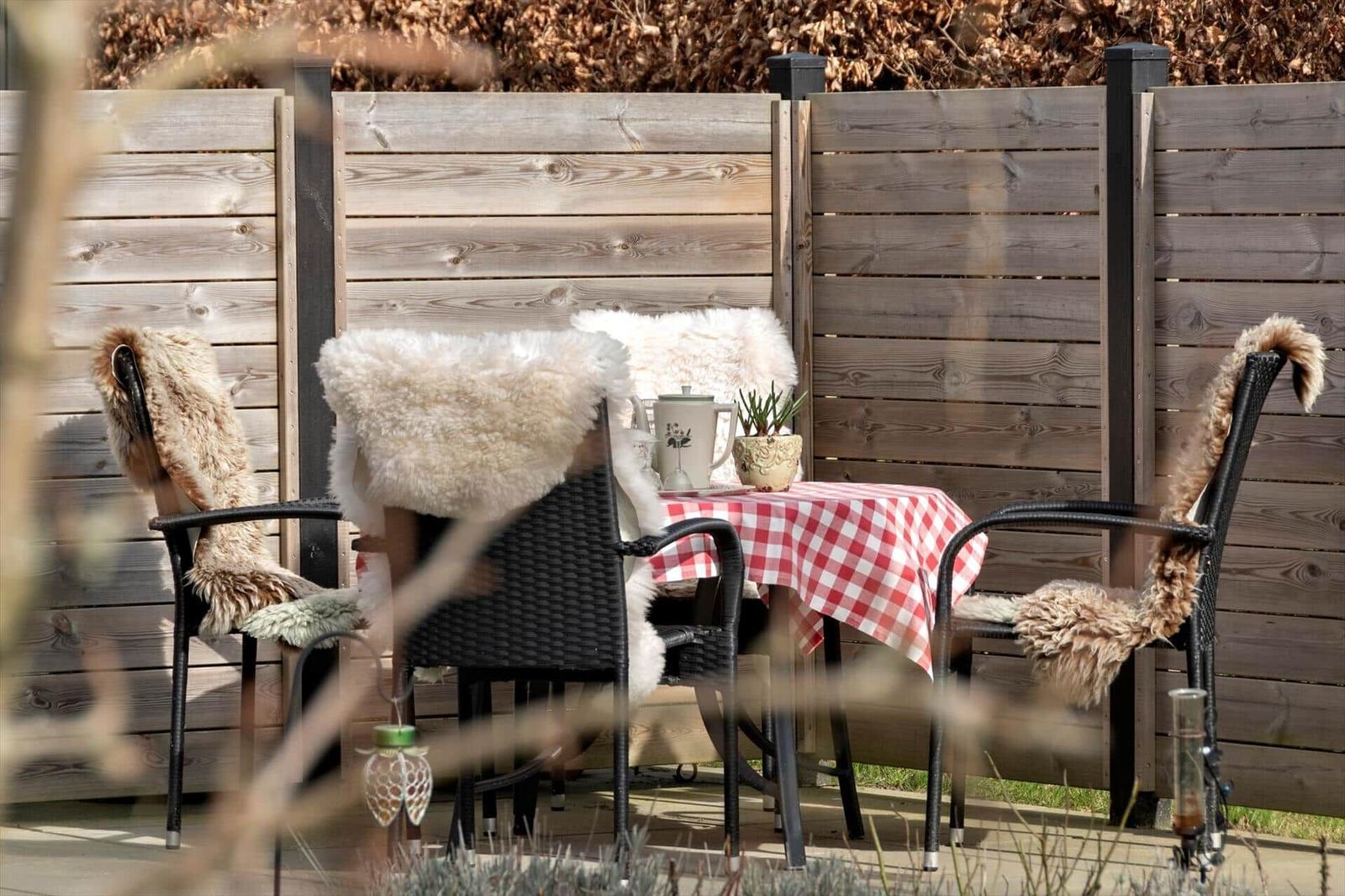 Terrasse mit Tisch, drei Stühlen und rotem Tischtuch.