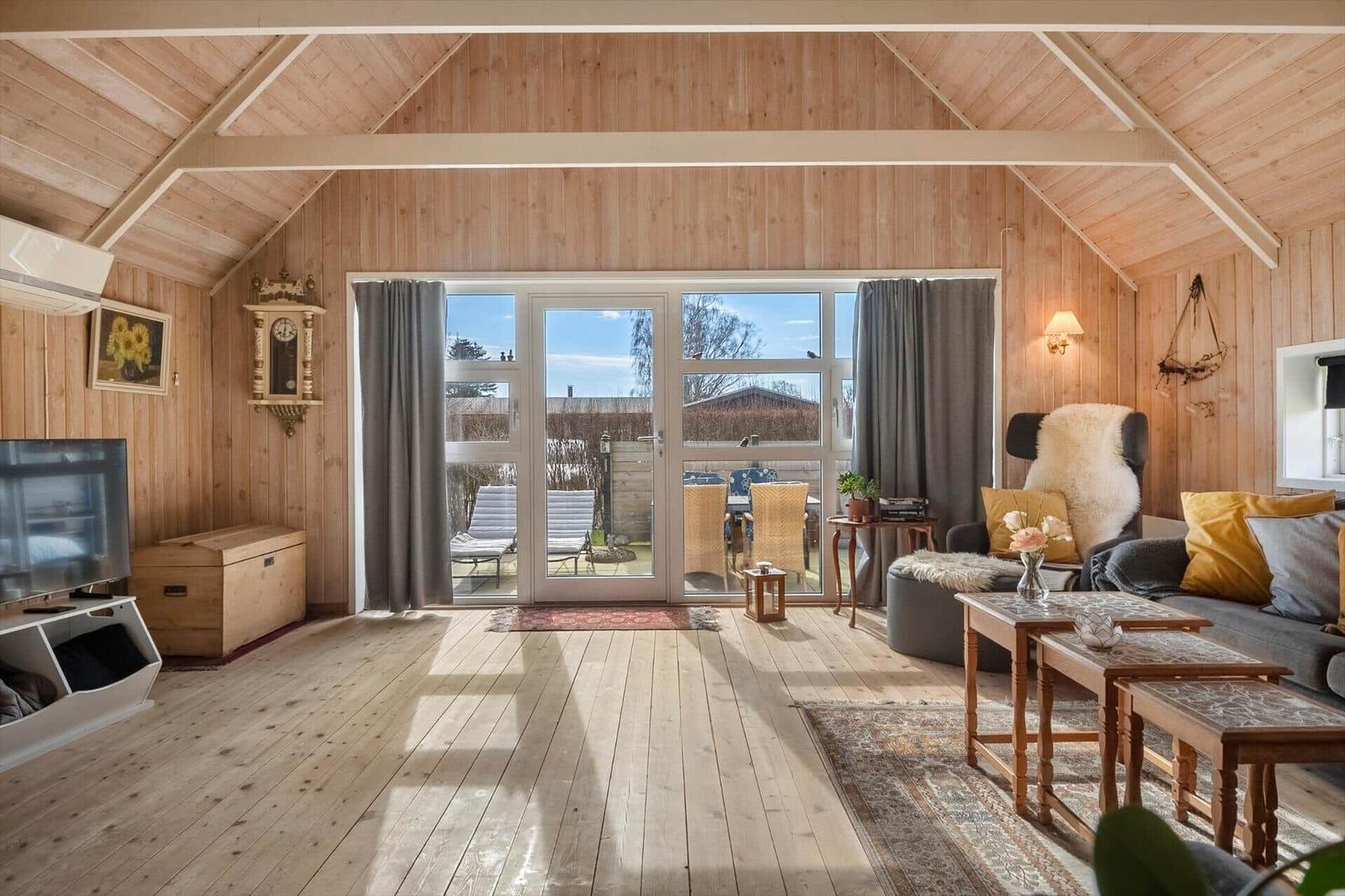 Wohnzimmer mit Holzdecke, Glasfront und Sofa mit Kissen.