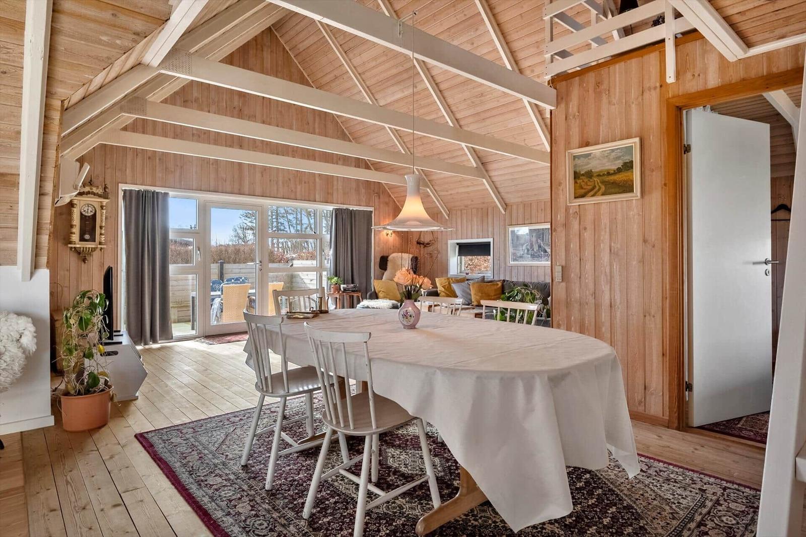 Ein Esszimmer mit Holzwand und -boden, großem Tisch und Sicht auf die Terrasse.