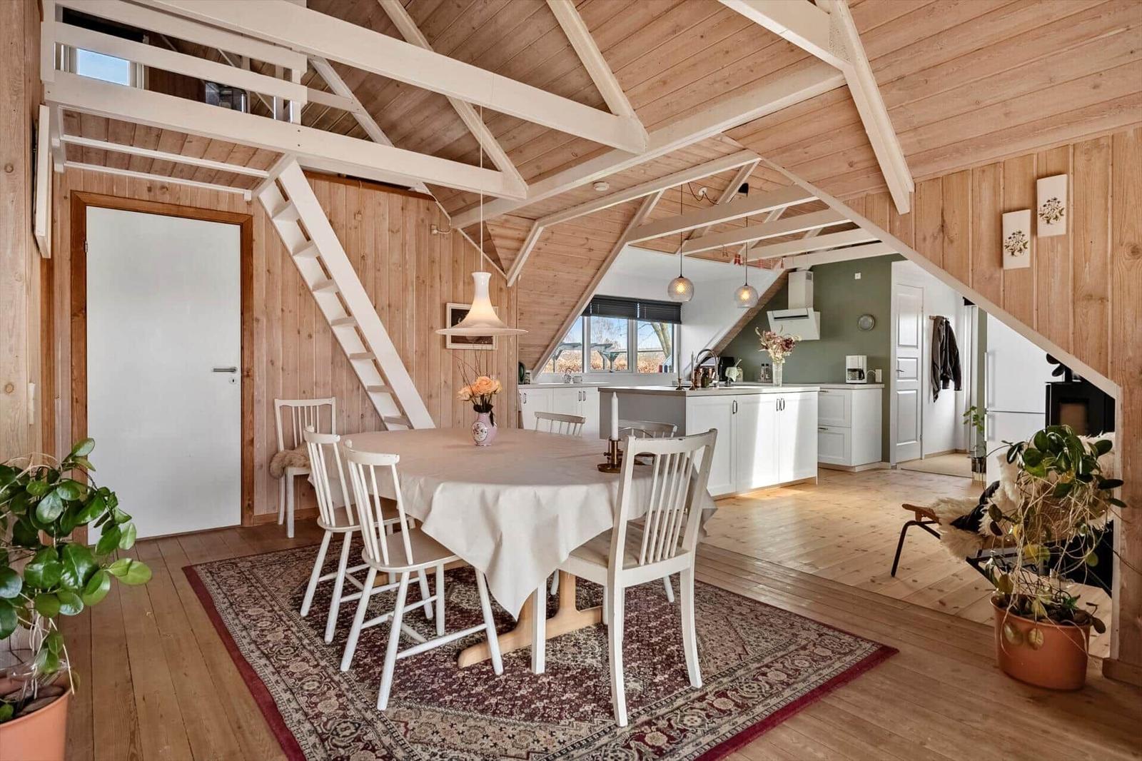 Essbereich mit Tisch und Stühlen unter Holzdecke. Küche und Wohnbereich im Hintergrund.