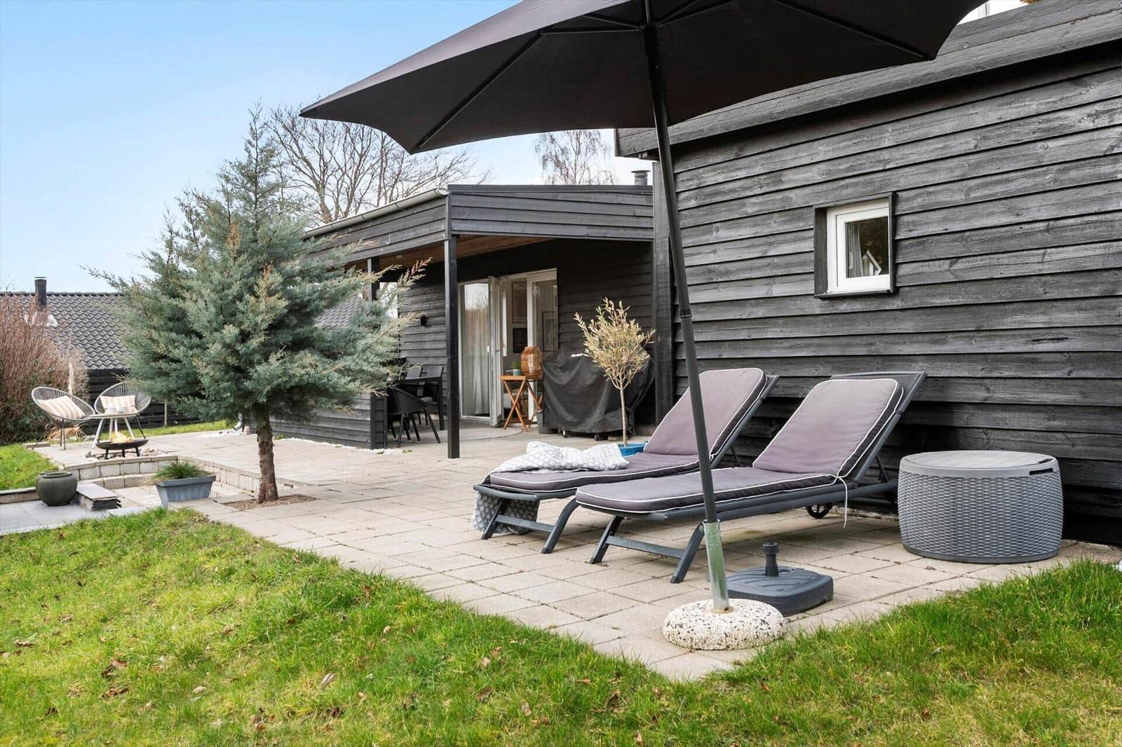 Terrasse mit Liegestühlen, Sonnenschirm und Gartenhaus mit Holzfassade.