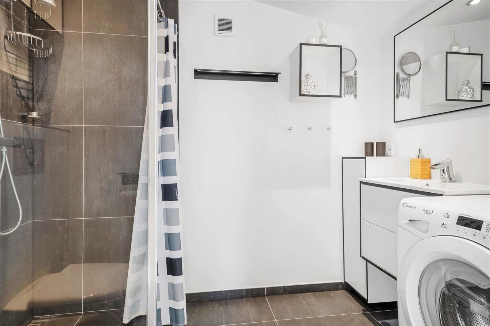Badezimmer mit Dusche, Waschmaschine und Spiegelschrank.