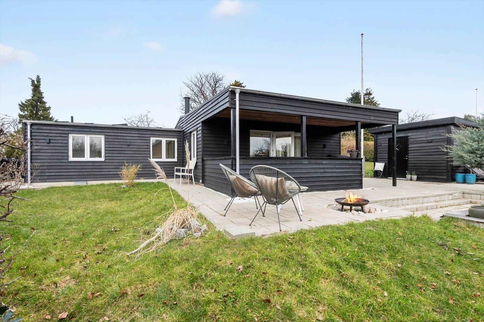 Moderne Villa mit Terrasse, Sitzgelegenheiten und Feuerkorb im Garten.