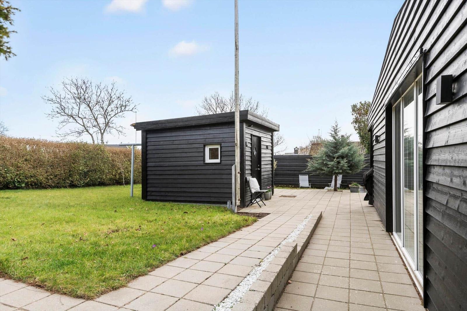 Hinterhof mit Pavillon, Terrasse und Rasenfläche. Schwarze Holzfassade und Bäume sichtbar.