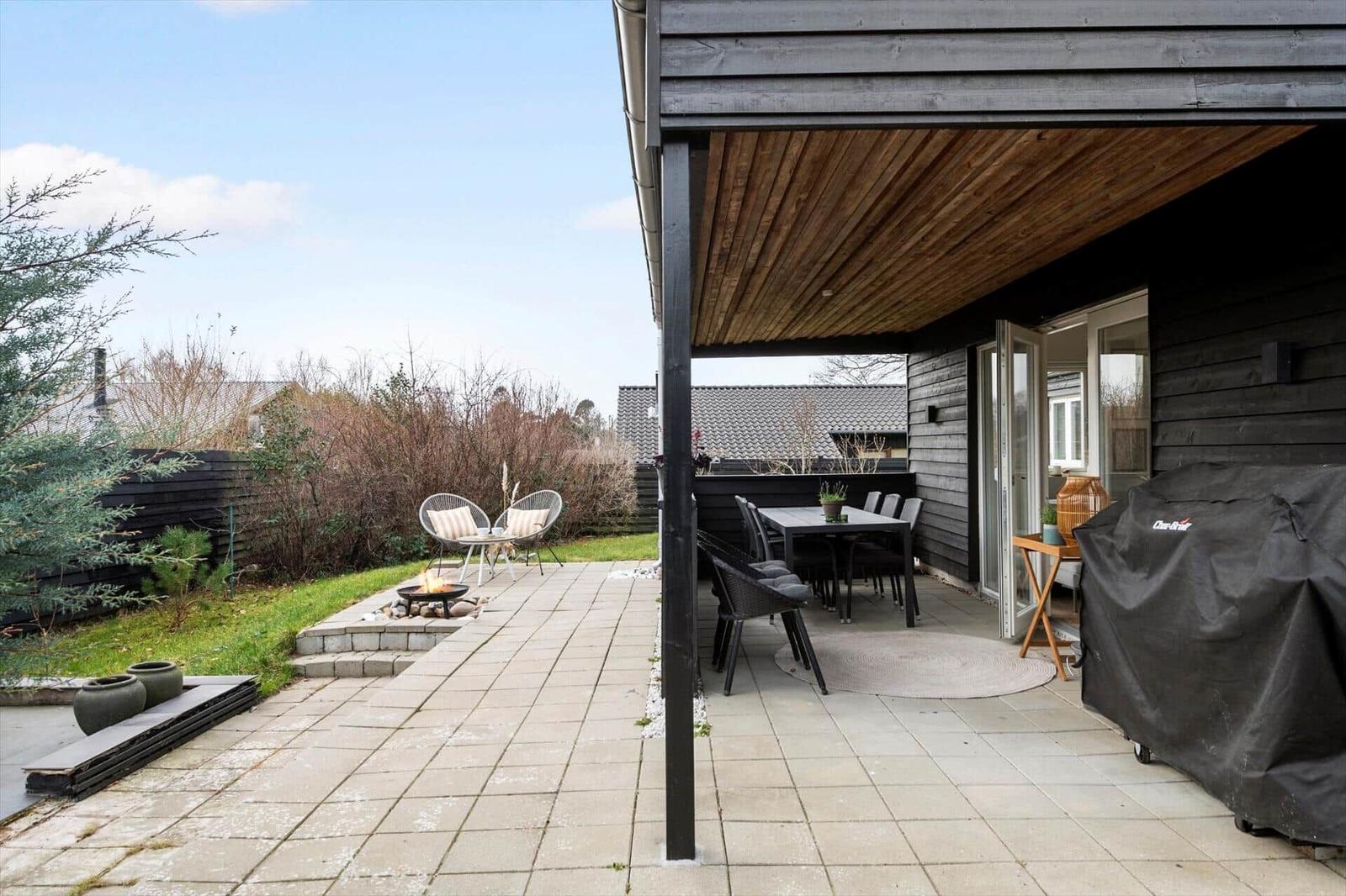 Terrasse mit Sitzgruppe, Esstisch und Grill. Außendiele mit Feuerkorb und Pflanzen.