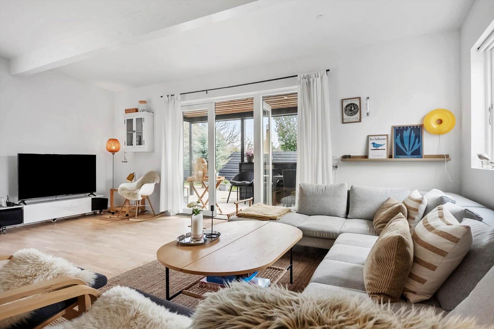 Wohnzimmer mit Sofa, Couchtisch und TV. Durchgang zur Terrasse mit Garten.